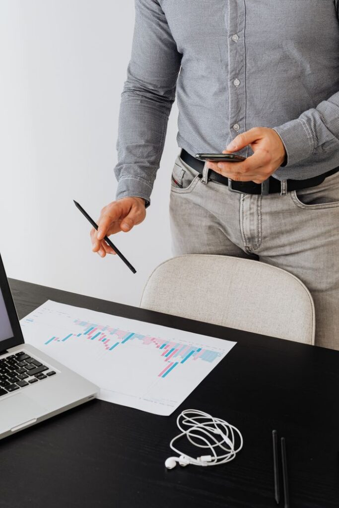 Man in office reviewing charts and using smartphone, concept of data analysis and technology.